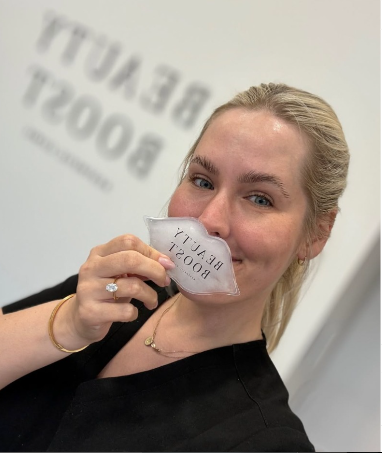 Woman holding an arnicare ice pack with 'BEAUTY BOOTY' branding in front of a white wall.