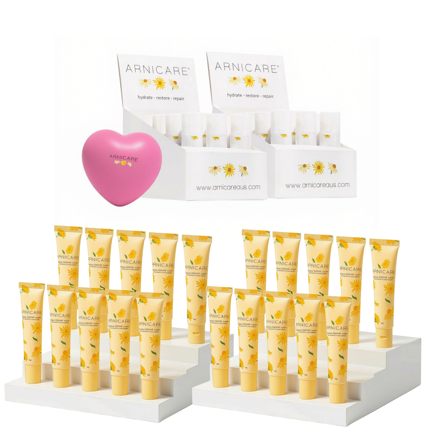 A set of Arnicare skincare products arranged on white display stands against a white background, including several small white tubes with yellow floral labels, a pink heart-shaped item, and branded display boxes.