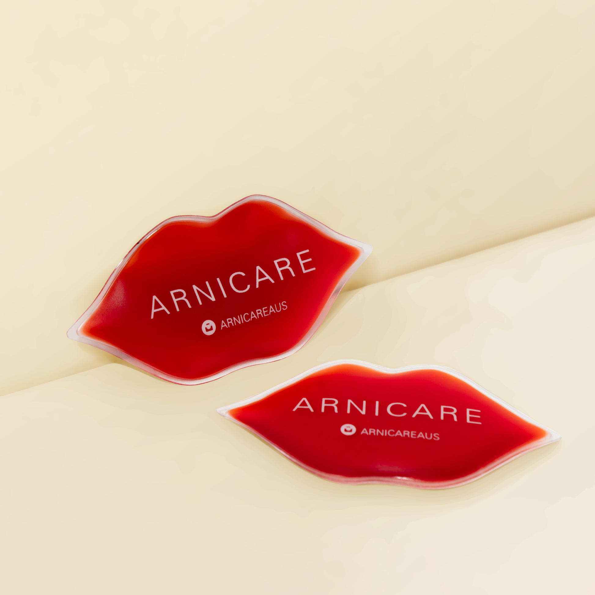 Two red lip-shaped cosmetic pouches with white ARNICARE branding, arranged on a warm cream background.