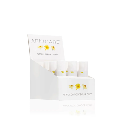 A white ARNICARE product display box containing several small white Arnicare Healing Balms with yellow daisy illustrations, photographed on a clean white background.