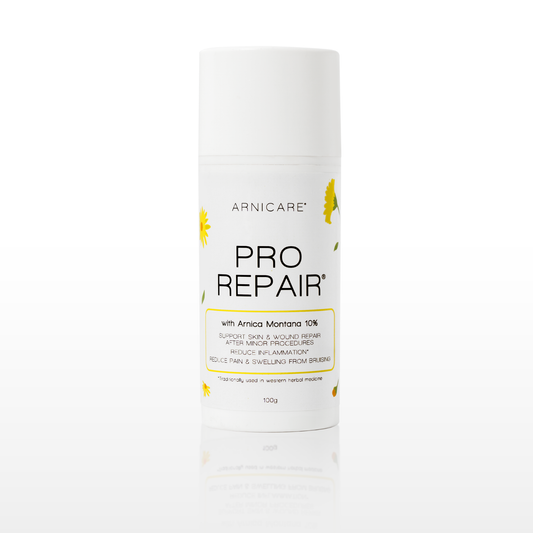 A white cylindrical cosmetic bottle of Arnicare Pro Repair with Amrica Montana 10% support skin and scar repair, featuring yellow daisy illustrations on a clean white background with a soft reflection.