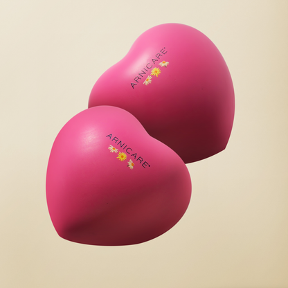 Two heart-shaped pink stress balls with the ARRNICARE brand name and yellow flower logo, displayed on a light beige background.